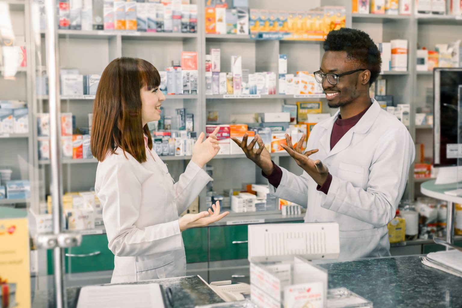 Portrait of multiethnical male and female pharmacists standing near pharmacy counter, talking